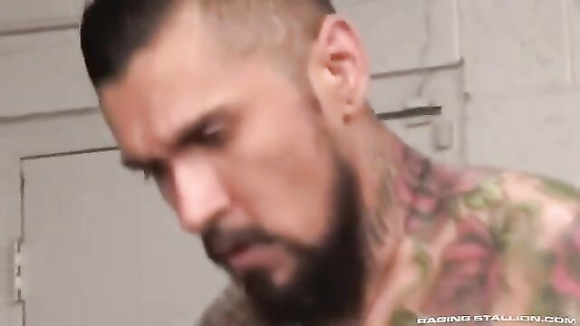 Tattooed muscular man with beard in shed, intense gaze