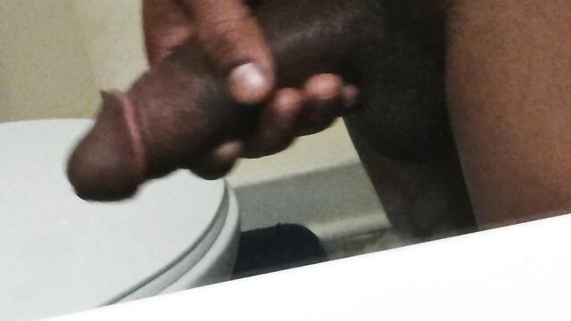Closeup of dark-skinned man gripping thick erect black cock in bathroom