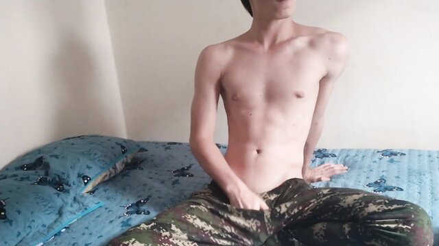 Skinny barely legal twink sits shirtless in camo pants on bed