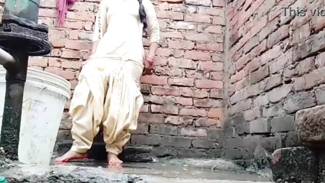 Desi Indian woman in white salwar kameez stands barefoot by water pump
