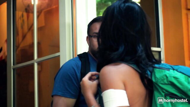 Black-haired woman with bandaged shoulder in skimpy top flirts with man at hotel door