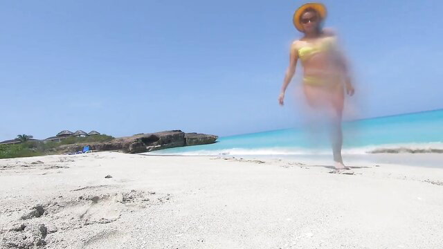 Blurry nude woman in yellow hat walks on Cuban beach by turquoise ocean