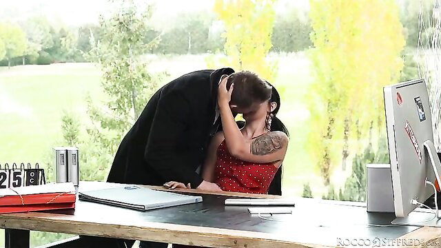Tattooed brunette kissed passionately by suited man in office