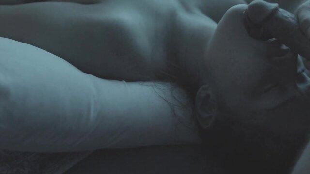 Bald woman lying nude on bed, hand stroking large cock close-up