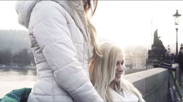 Angella Christin smiling on Charles Bridge at sunset, blonde beauty in white coat