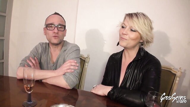 Blonde MILF Sophia in leather top with man at table, adult tease