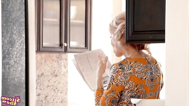 Blonde redhead stepmom in floral dress reading newspaper in kitchen