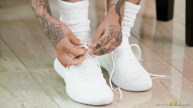 Tattooed woman tying white sneakers, thick thighs in wool socks