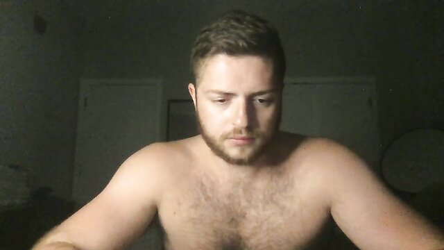 Muscular hairy bearded guy shirtless in dim bedroom glow