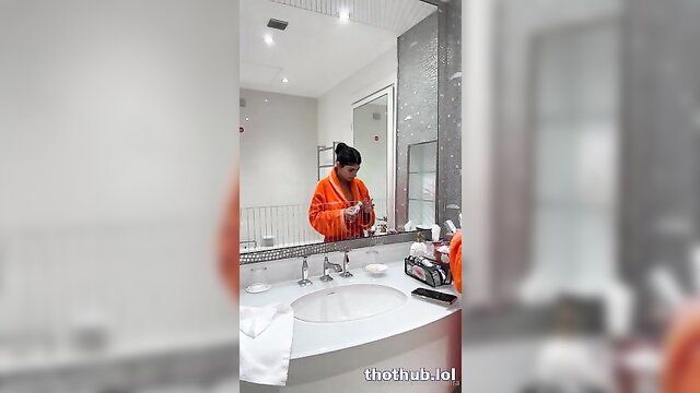 Mia Khalifa in orange jumpsuit brushing teeth in mirror, sexy bathroom tease