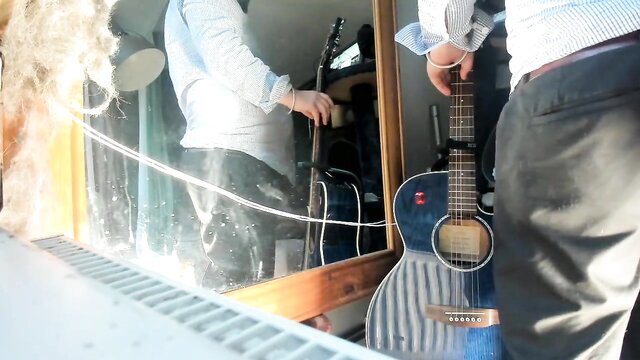 Man in white shirt and slacks stands by mirror with guitars in music room