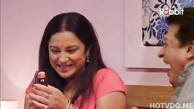 Smiling Indian Bhabhi in pink saree holds bottle, flirty glance