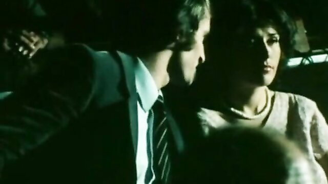 Retro 70s couple in car: suited man kisses brunette woman close-up