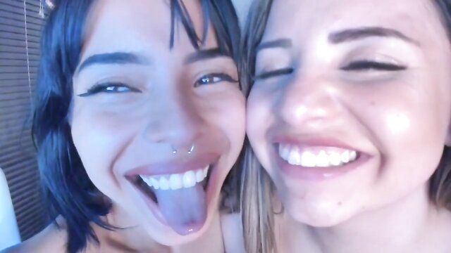 Two smiling Latina lesbians in close-up eye contact selfie, tongues out