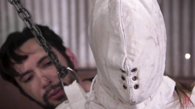 Woman in white bondage hood chained, man prepares for canning and anal fuck