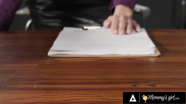 Reagan Foxx in leather skirt holds clipboard at desk in Mommy's Girl scene