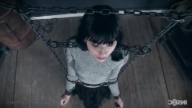 Beautiful girl in tight bondage, suspended by chains in sexy sweater and skirt