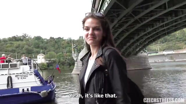 Hot Czech brunette in leather jacket by river bridge, smiling seductively
