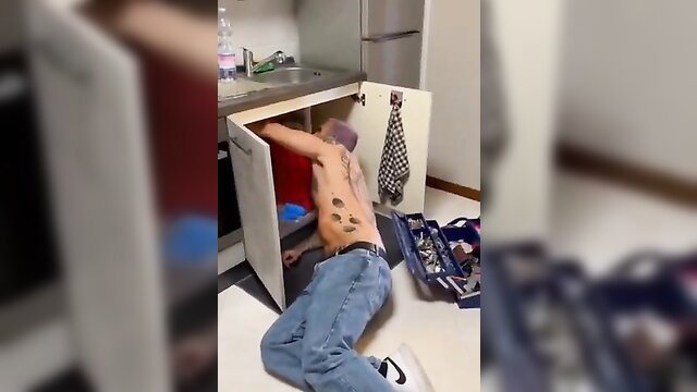 Tattooed man under sink with pants down, bulge visible, amateur repair blowjob tease