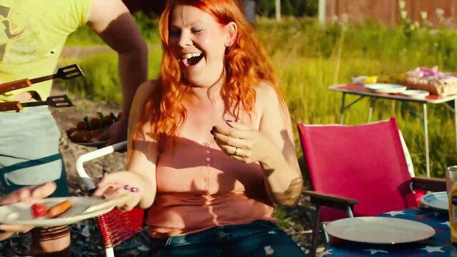 Redhead Eeva Soivio laughs at outdoor BBQ with sausage in hand