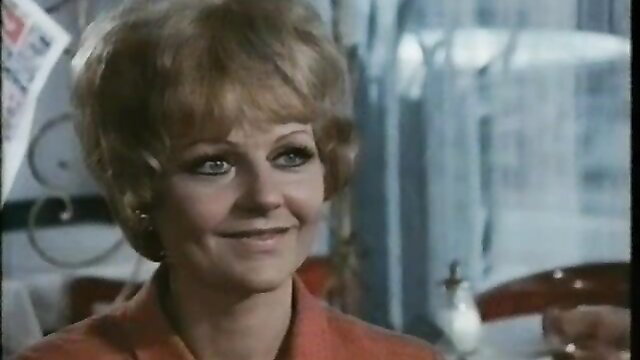 Blonde retro 70s housewife smiling in orange dress, softcore Hausfrauen-Report