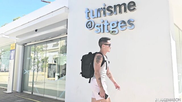 Tattooed Asian twink in shorts outside Sitges tourism office