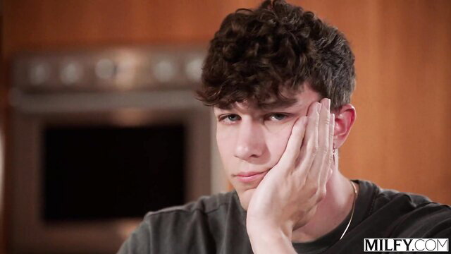 Curly-haired young guy resting face in hand, Milfycam kitchen scene