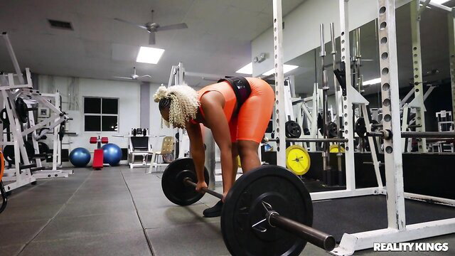 Blonde black babe in orange shorts deadlifting at gym, thick ass up