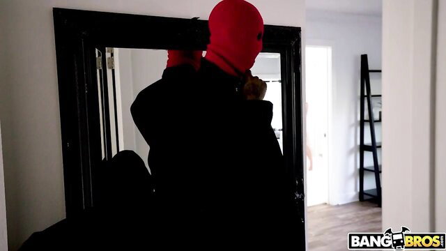 Masked man in red balaclava adjusts outfit in mirror, Bang Bros adult scene