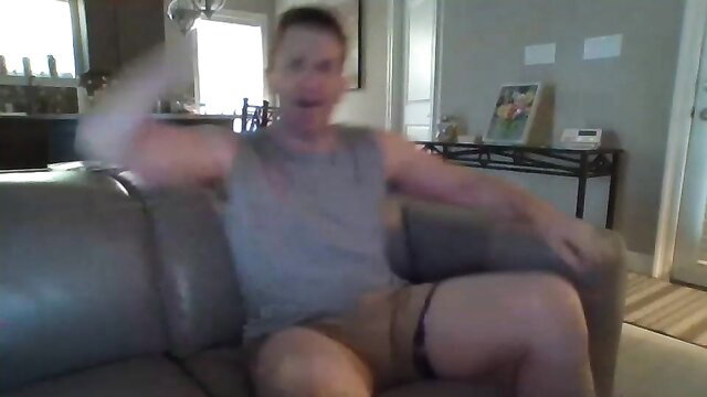 Muscular white guy in tank top and shorts flexing on couch in gay amateur video