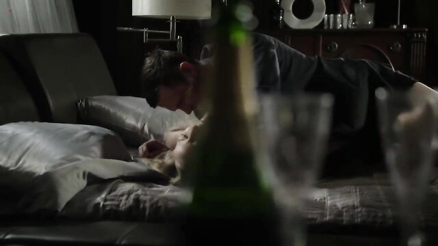 Blonde seductress kissing man passionately on bed in softcore scene