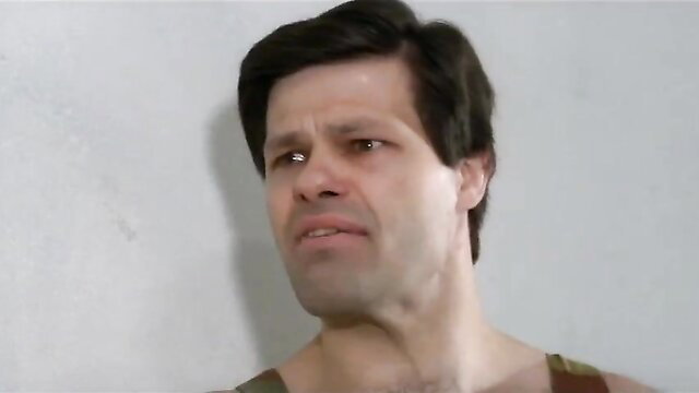 Muscular man in tank top with intense stare in prison group shower scene