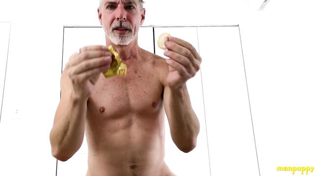 Nude muscular silver daddy holds condom and pill in lewd feed tease