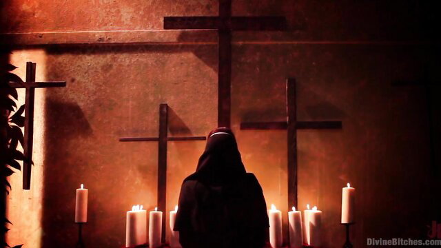 Sexy redhead nun in dark robe before crosses and candles in divine chapel