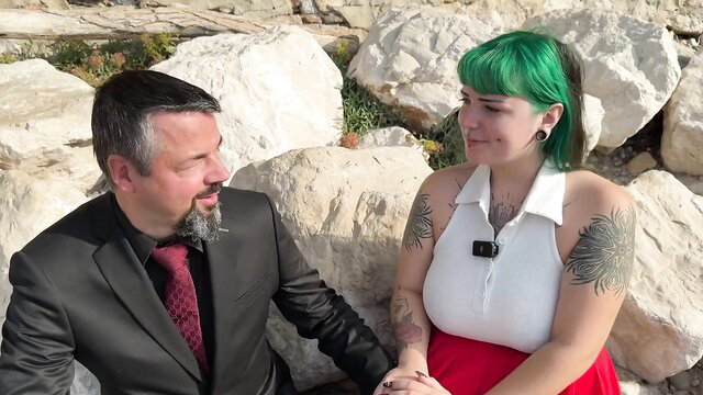 Lilith 20yo green-haired student with tattoos smiles with suited man on rocks