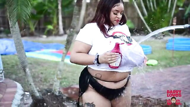 Curvy black woman in wet white t-shirt, soaked with water outdoors