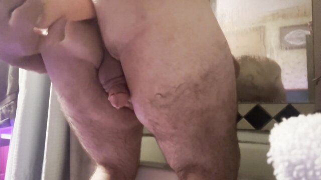 Mature man in shower holds small penis and dildo near tight ass