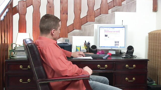 Man in red shirt sits at desk typing on old computer monitor