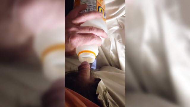 Man pouring Nesquik from bottle onto erect cock in bed
