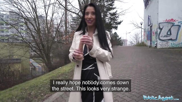 Brunette in coat on public street holds dildo nervously hoping no one sees