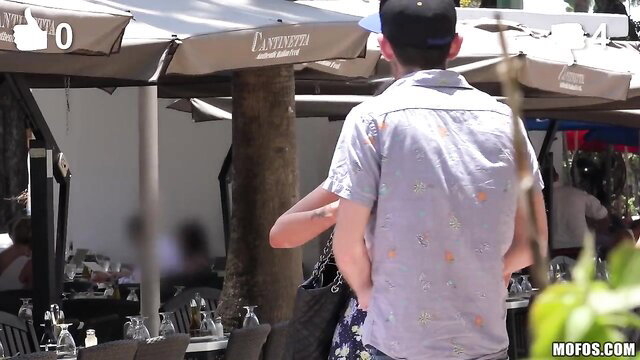 Gia Paige in floral shirt and shorts hugs guy at outdoor cafe