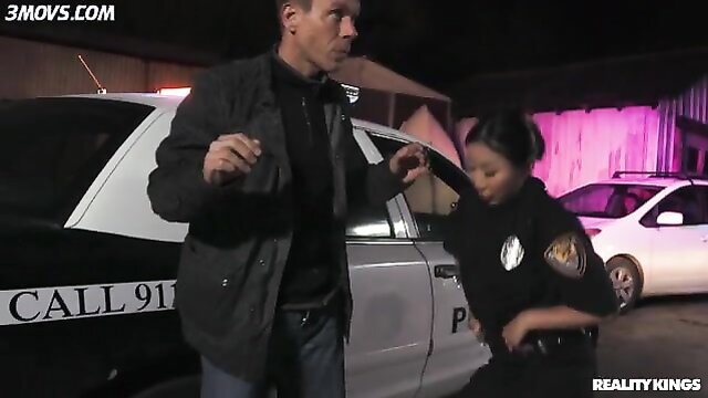 Nicole Doshi in cop uniform with Mick Blue by police car outdoors