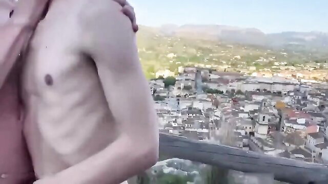 Two cute slim guys embracing nude outdoors with city view
