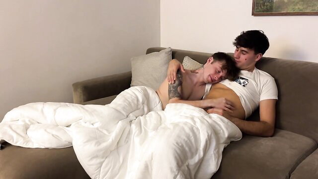 Cute tattooed gay couple cuddling intimately under blanket