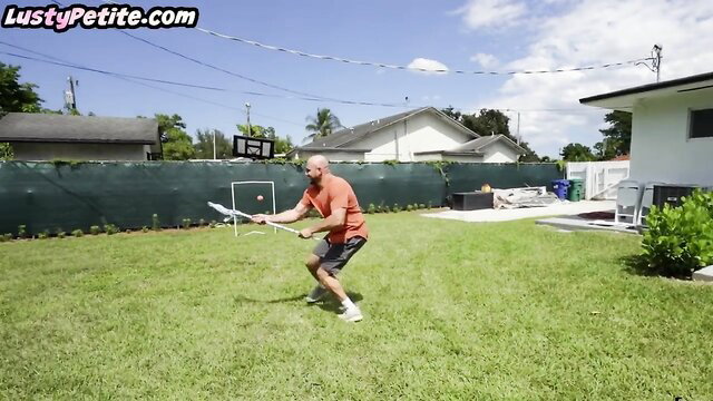 Bald tanned man playing tennis in backyard wearing shorts