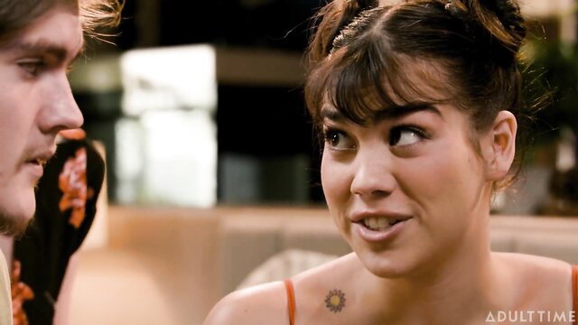 Brunette beauty in orange top chats intimately with man in steamy scene