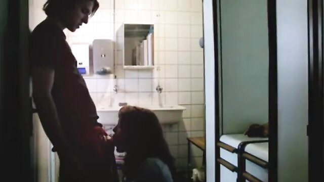 Skinny brunette actress kneels giving oral to tall man in bathroom