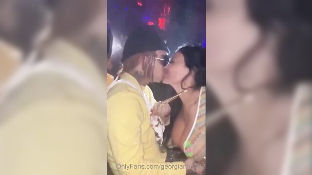 Blurry leaked OnlyFans couple kiss in club, man in yellow hat sunglasses, woman with dark hair cleavage