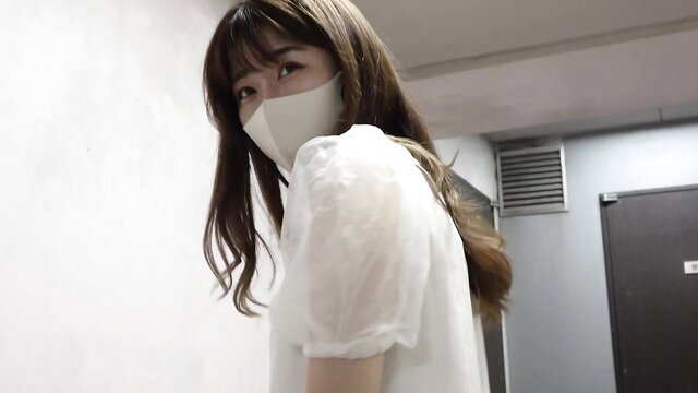 Asian beauty in sheer blouse and mask glances back seductively