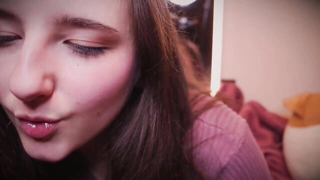 AftynRose ASMR disrobing for couch, a young woman with long brown hair and pink lips, slightly parted and glistening